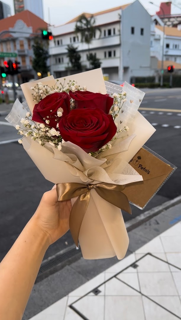 A hand holds a beautifully wrapped bouquet of red roses and baby's breath from Cool Petals.