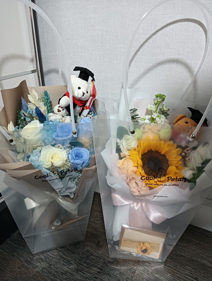 Two beautifully arranged flower bouquets in clear bags, one featuring a graduation teddy bear.