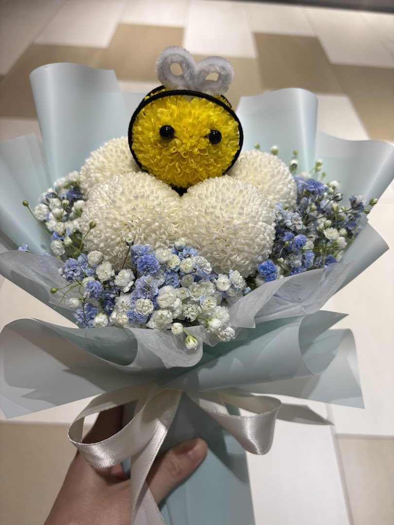 A charming bouquet featuring white flowers, blue baby's breath, and a cute yellow bee character.
