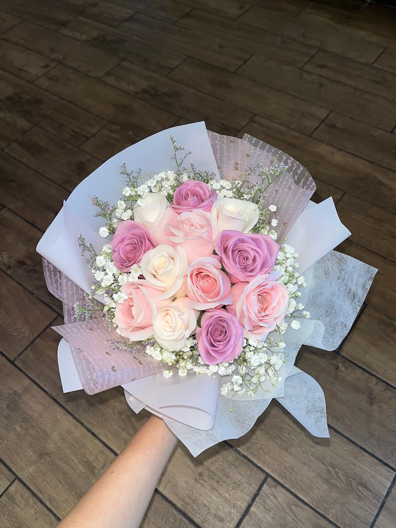 A beautiful bouquet of pink, purple, and white roses with baby's breath, elegantly wrapped.