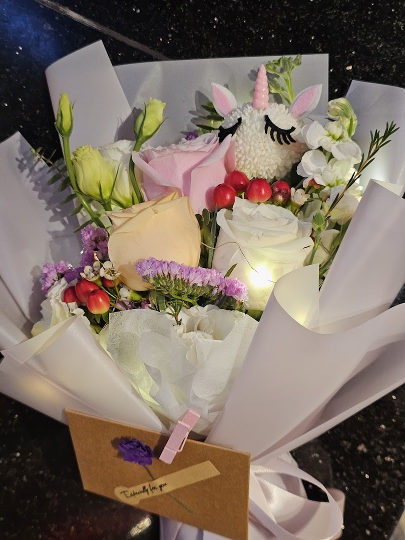 A charming floral bouquet featuring roses, berries, and a whimsical unicorn, illuminated by soft lights.