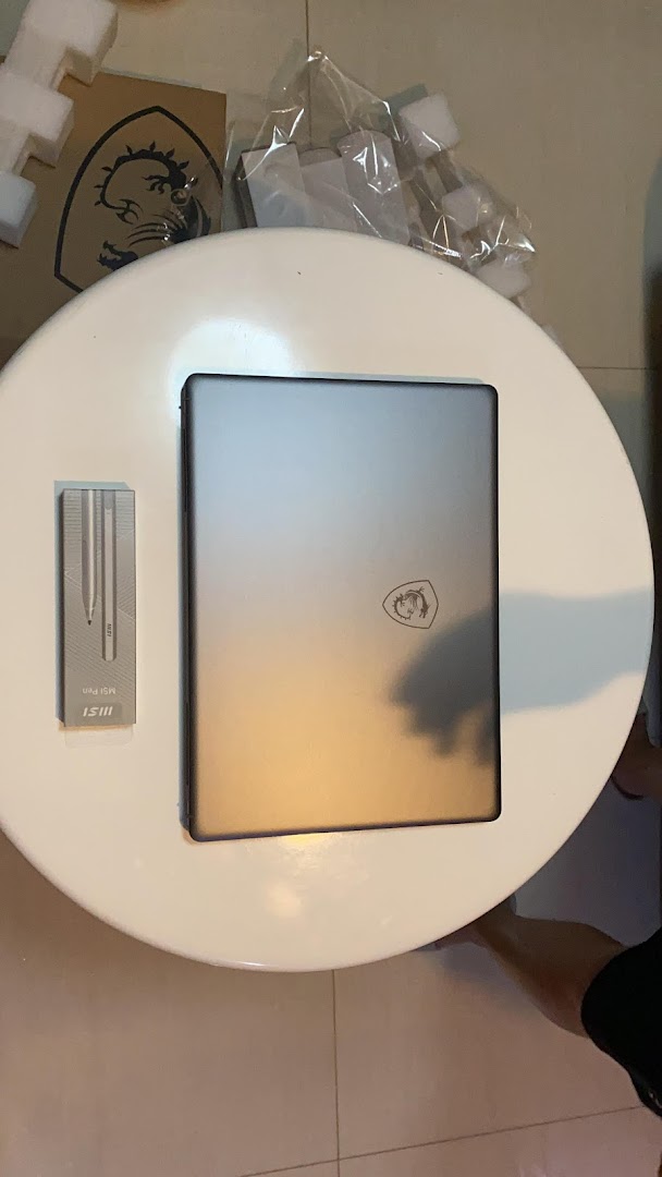 An MSI laptop and pen on a white table, with packaging materials in the background.