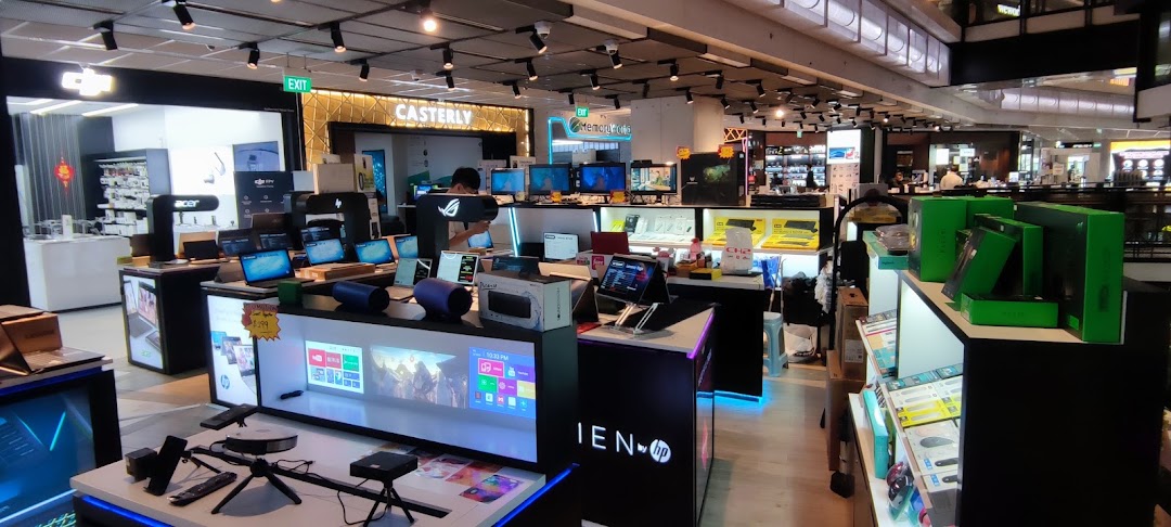 An electronics retail store interior showcasing various laptops, monitors, and tech accessories with a customer browsing.