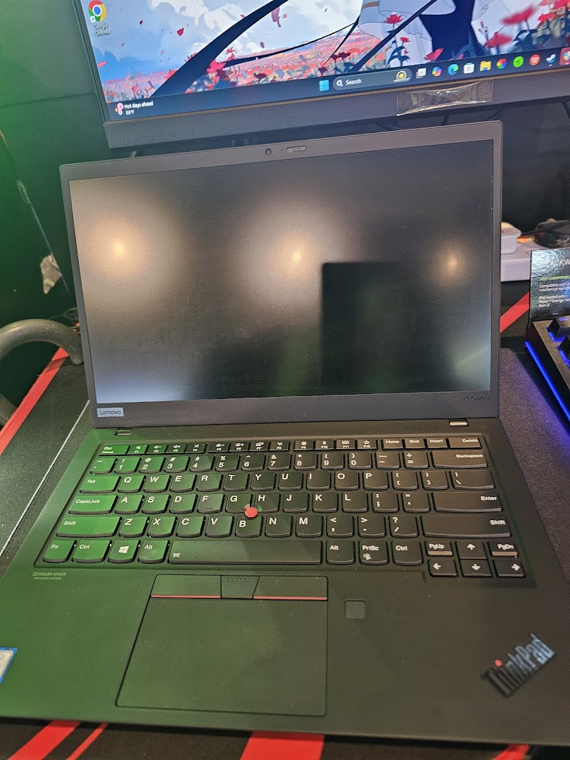 A close-up view of a black Lenovo ThinkPad laptop on a desk, with a monitor in the background.