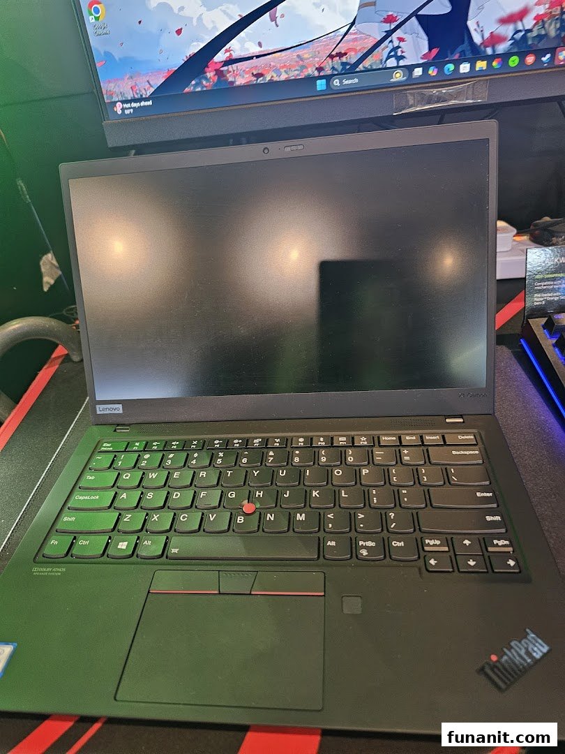 A close-up view of a black Lenovo ThinkPad laptop on a desk, with a monitor in the background.