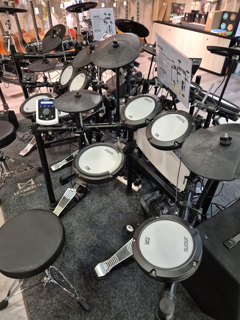 An array of electronic drum kits displayed in a music store, with guitars visible in the background.