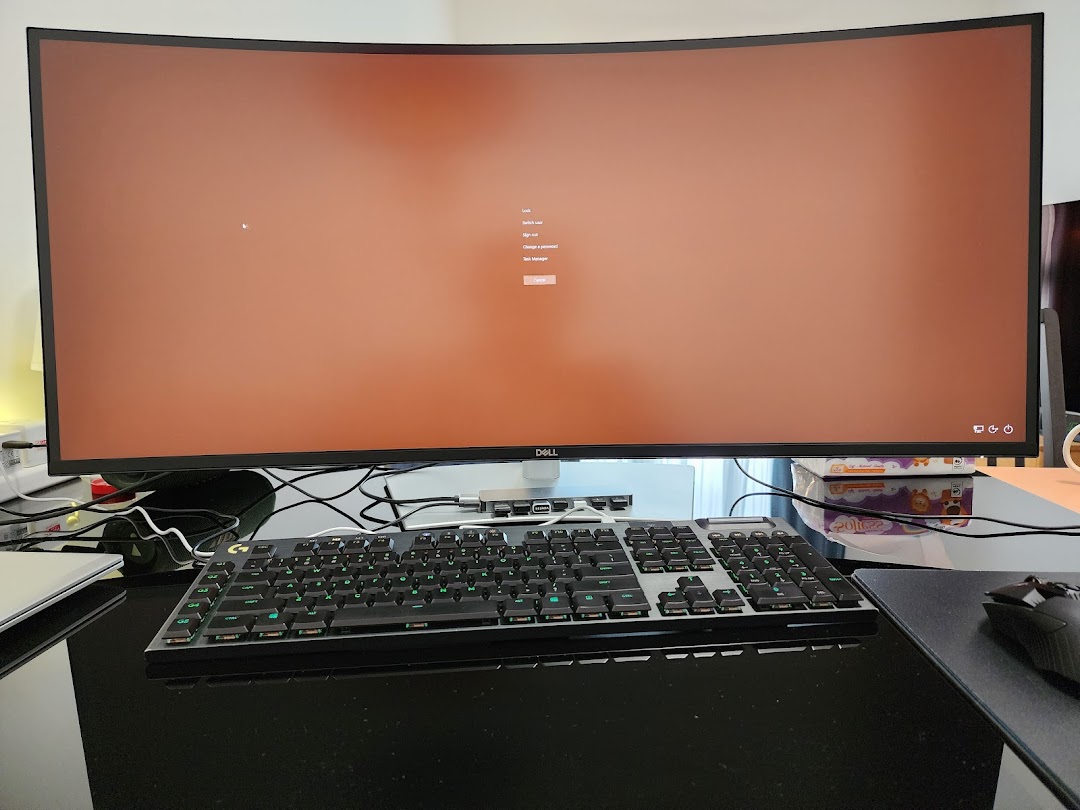 A large Dell curved monitor displaying a login screen, paired with a gaming keyboard and mouse on a desk.