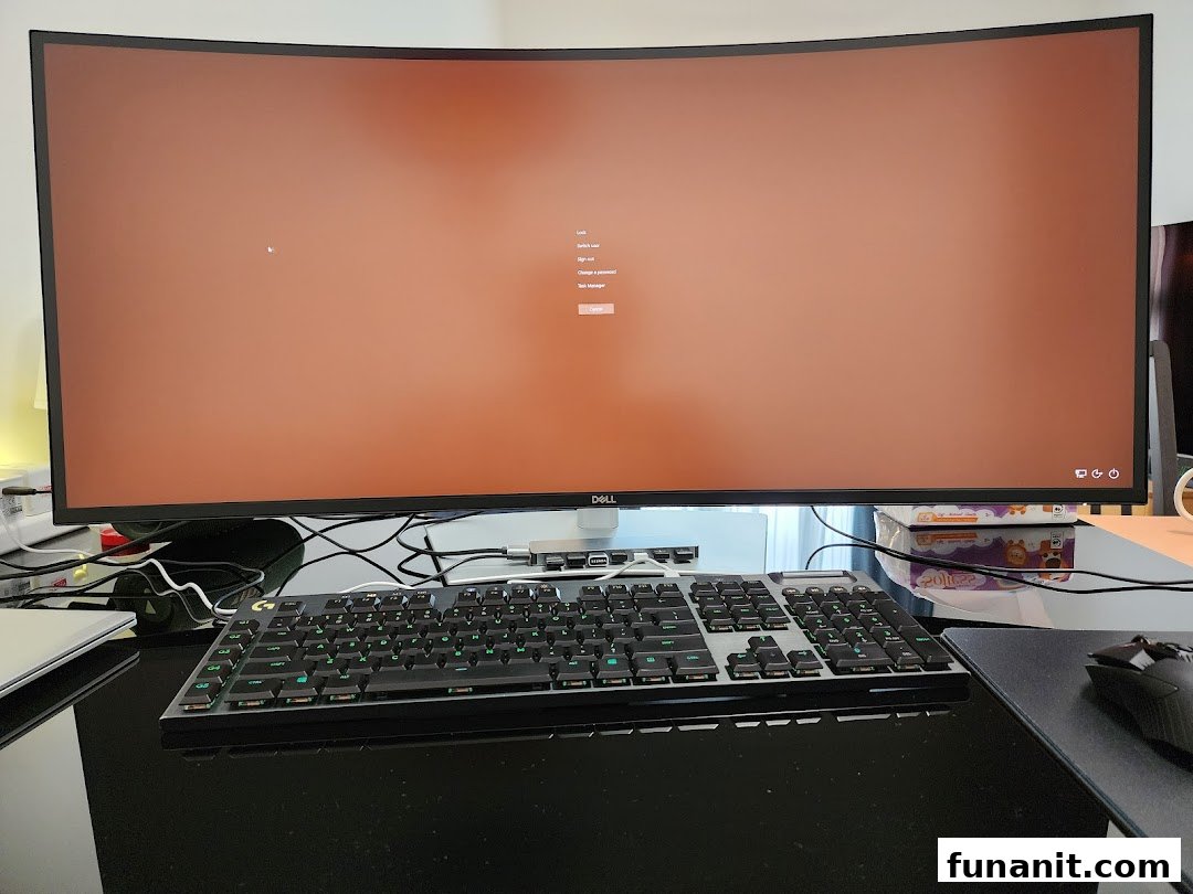 A large Dell curved monitor displaying a login screen, paired with a gaming keyboard and mouse on a desk.