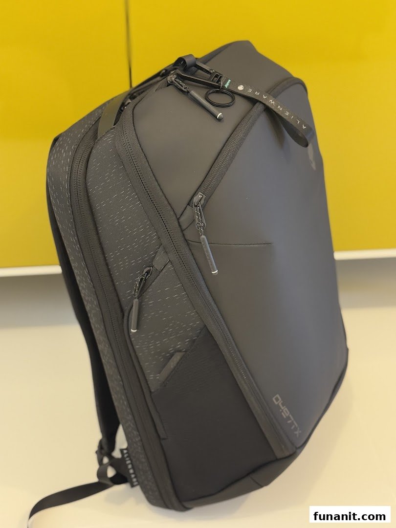 A sleek black Alienware backpack with multiple compartments and branding, displayed against a yellow wall.