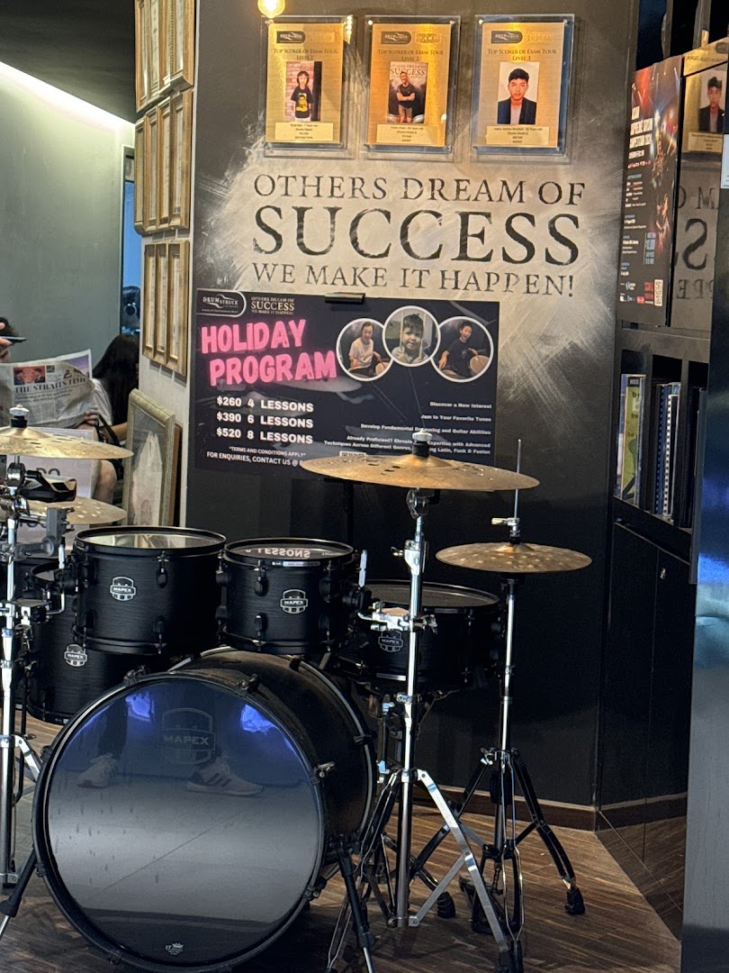 A drum set displayed next to a wall featuring a 'Holiday Program' poster with lesson prices.