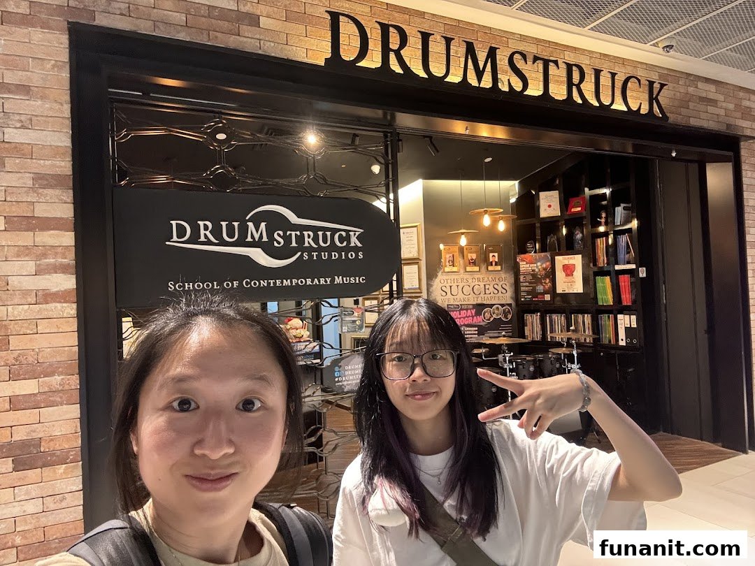 Two individuals pose in front of Drumstruck Studios, a school of contemporary music.