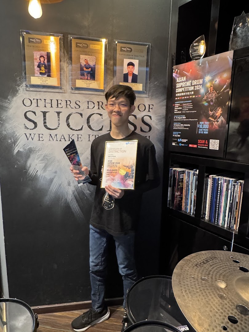 A young man proudly displays his drum competition award and certificate in a studio setting.