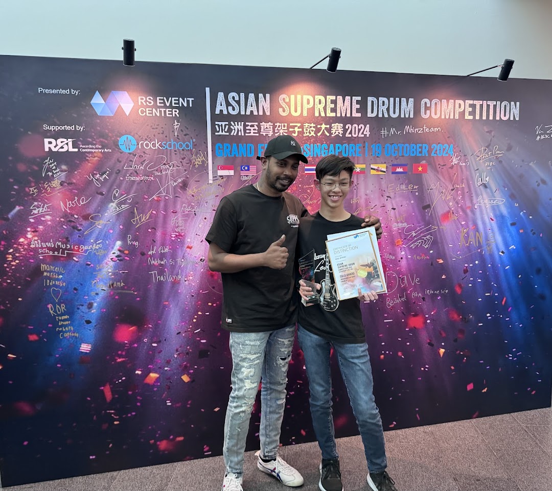 Two individuals celebrate an award at the Asian Supreme Drum Competition, showcasing drumming excellence.