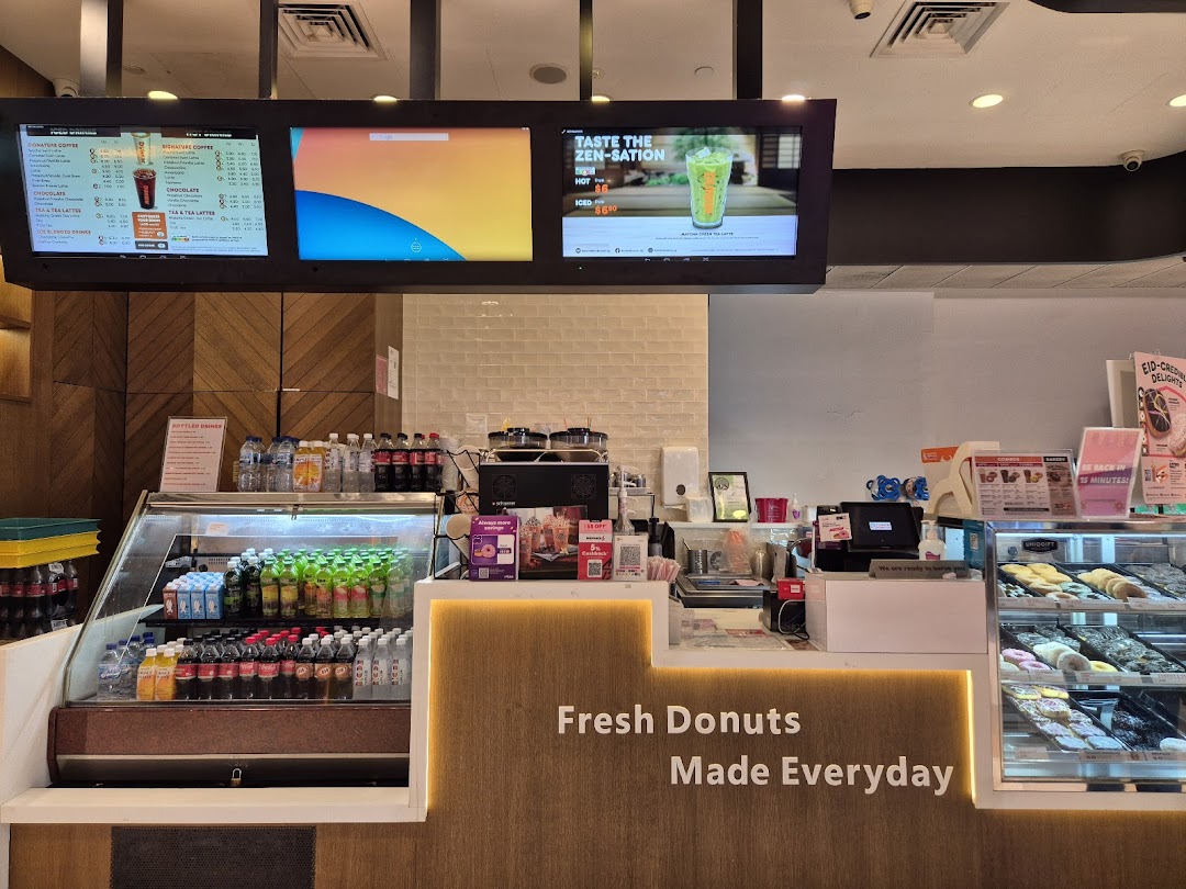 Interior view of Dunkin Donuts counter with fresh donuts, bottled drinks, and digital menu boards.