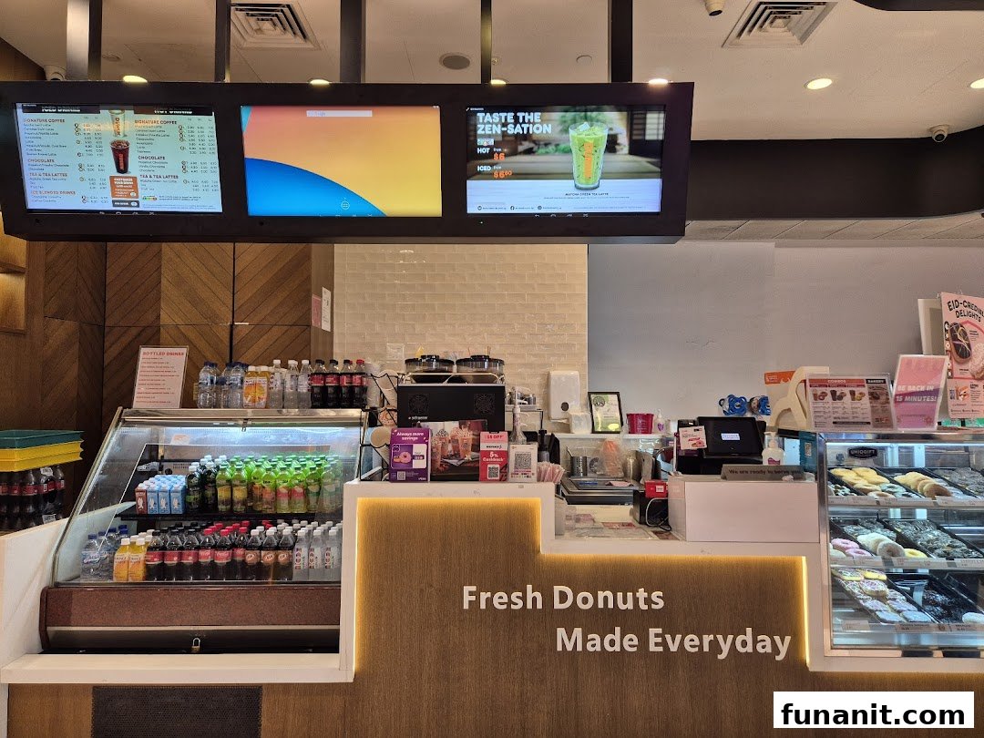 Interior view of Dunkin Donuts counter with fresh donuts, bottled drinks, and digital menu boards.