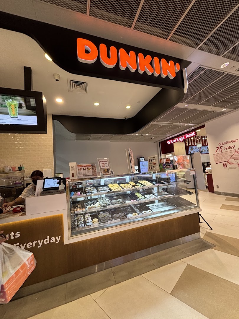 A vibrant Dunkin' Donuts counter showcasing a wide selection of fresh donuts and a staff member serving.