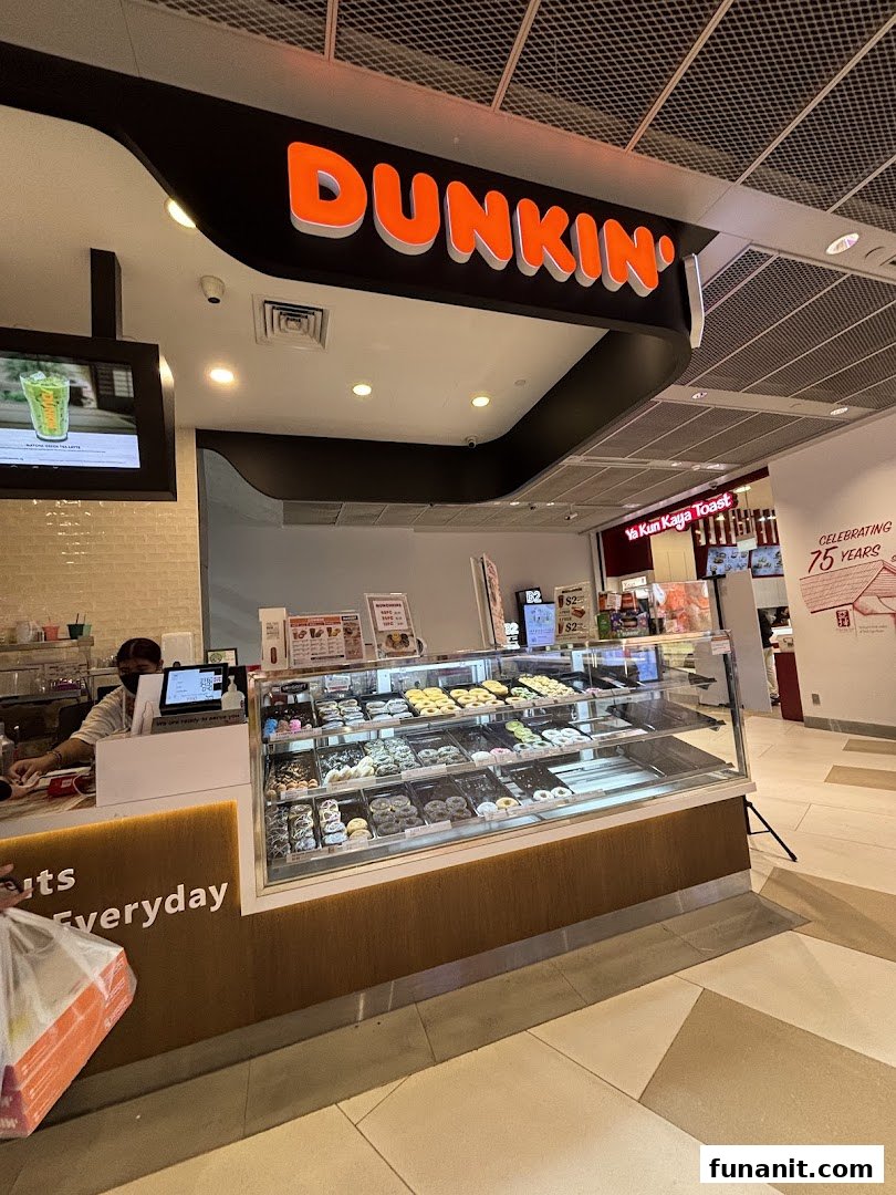 A vibrant Dunkin' Donuts counter showcasing a wide selection of fresh donuts and a staff member serving.