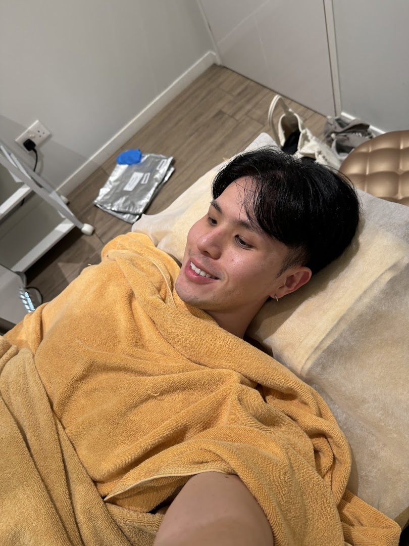 A man in a yellow towel smiles while relaxing on a treatment bed at Expressions Funan.