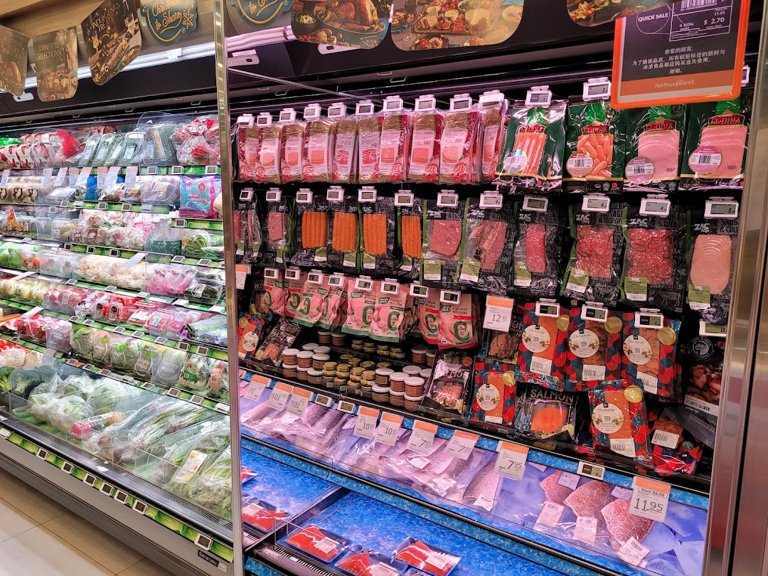 A well-stocked refrigerated section at FairPrice Finest, featuring fresh produce, deli meats, and seafood.