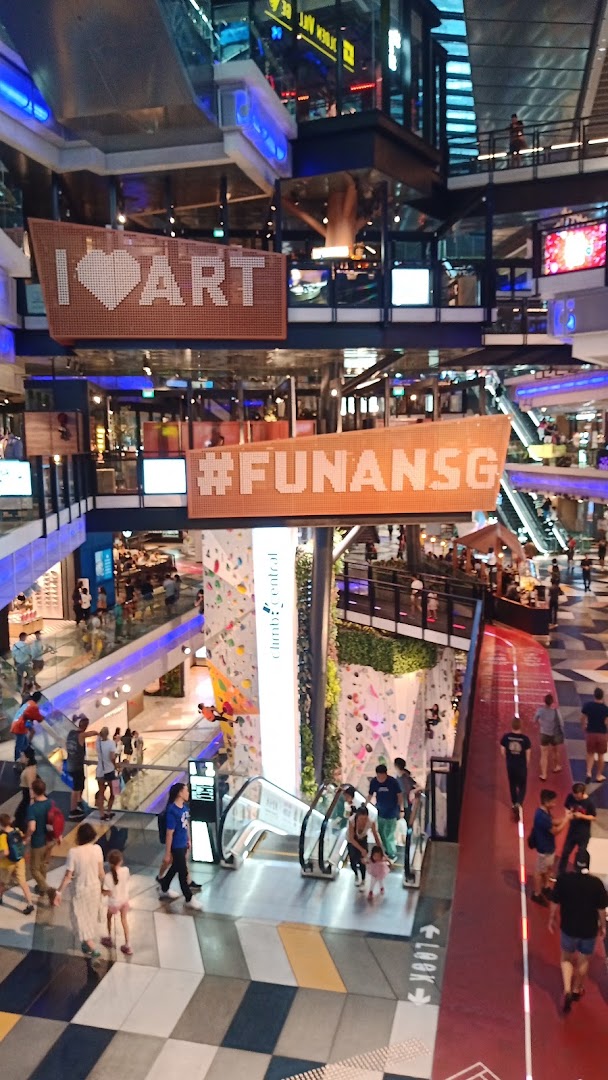 A vibrant multi-level mall interior with escalators, a climbing wall, and people exploring.