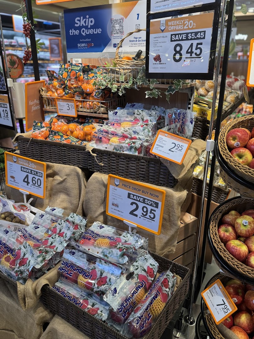 A vibrant display of fresh fruits, including oranges, apples, and grapes, with promotional offers at FairPrice Finest.