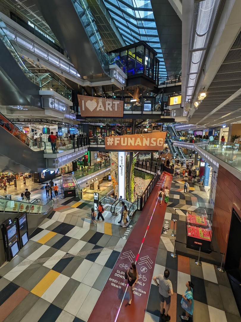 Vibrant multi-level mall interior with escalators, shops, a climbing wall, and a cycling path.
