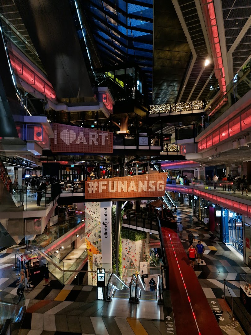 A vibrant multi-level interior of Funan Mall, featuring escalators, shops, and a prominent indoor climbing wall.