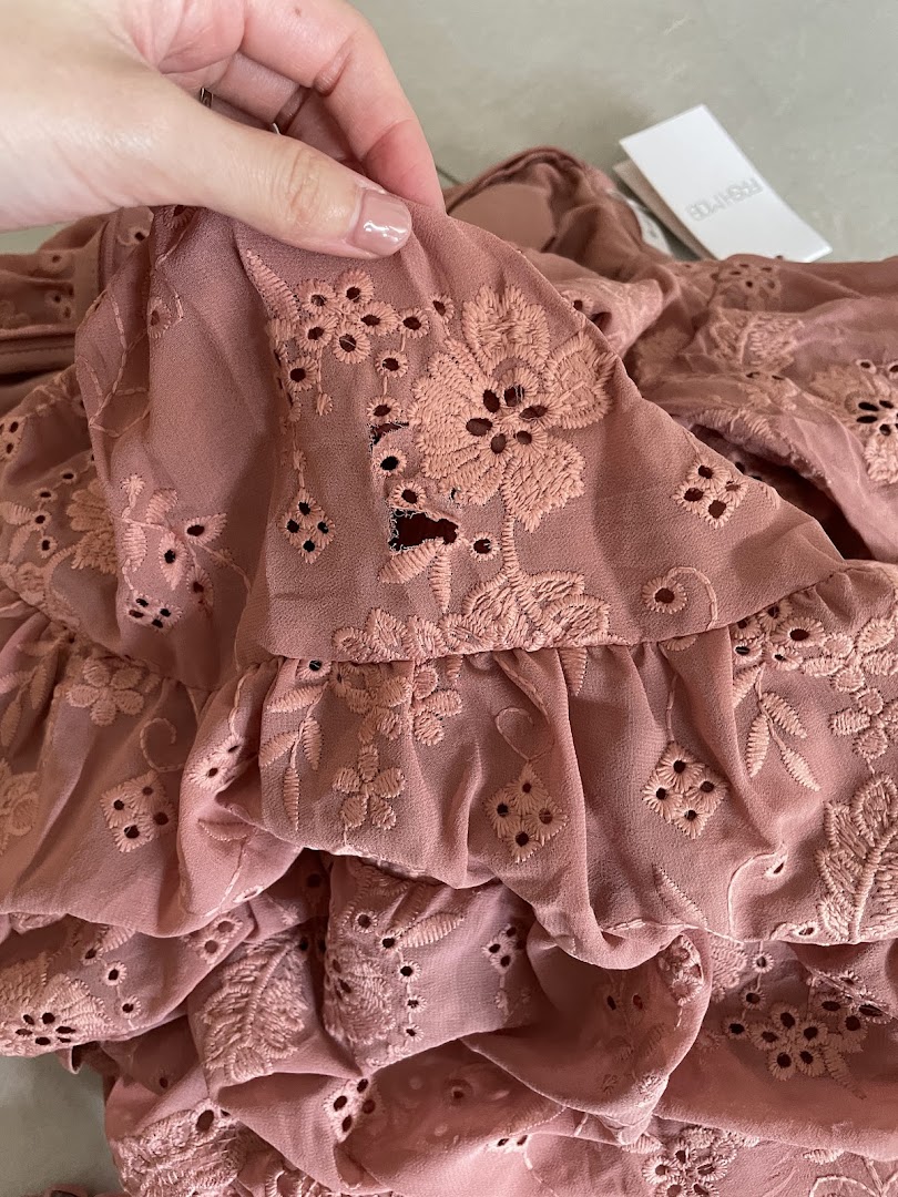 Close-up of a dusty rose fabric with intricate eyelet embroidery and ruffles, showcasing Fash Mob's design.