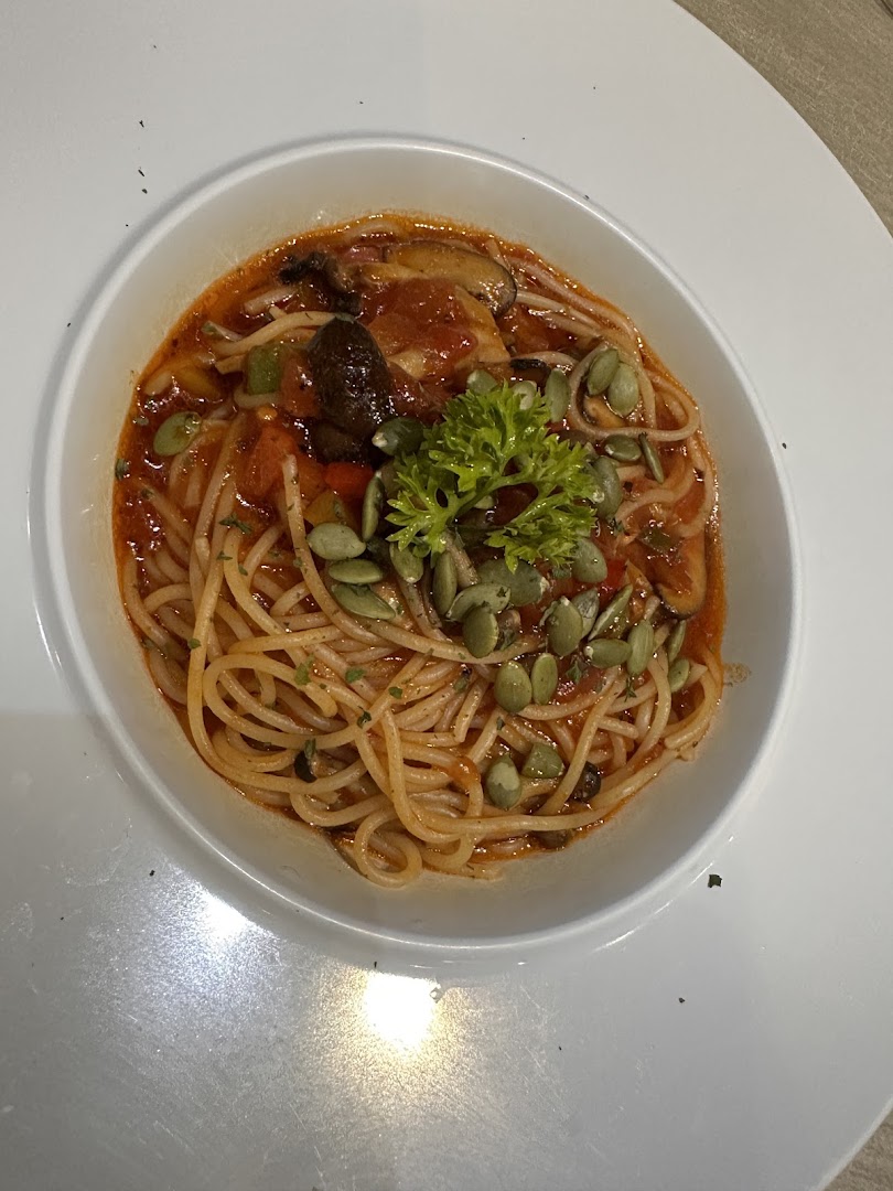 A vibrant bowl of spaghetti with tomato sauce, mushrooms, vegetables, and pumpkin seeds.