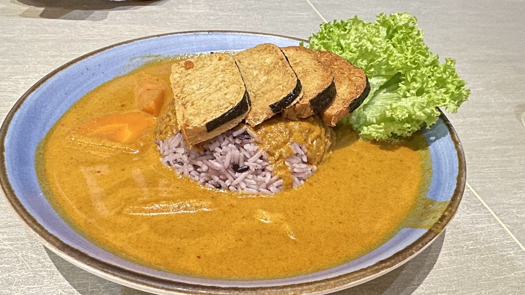 A vibrant plate of curry with purple rice, tofu slices, and fresh lettuce.