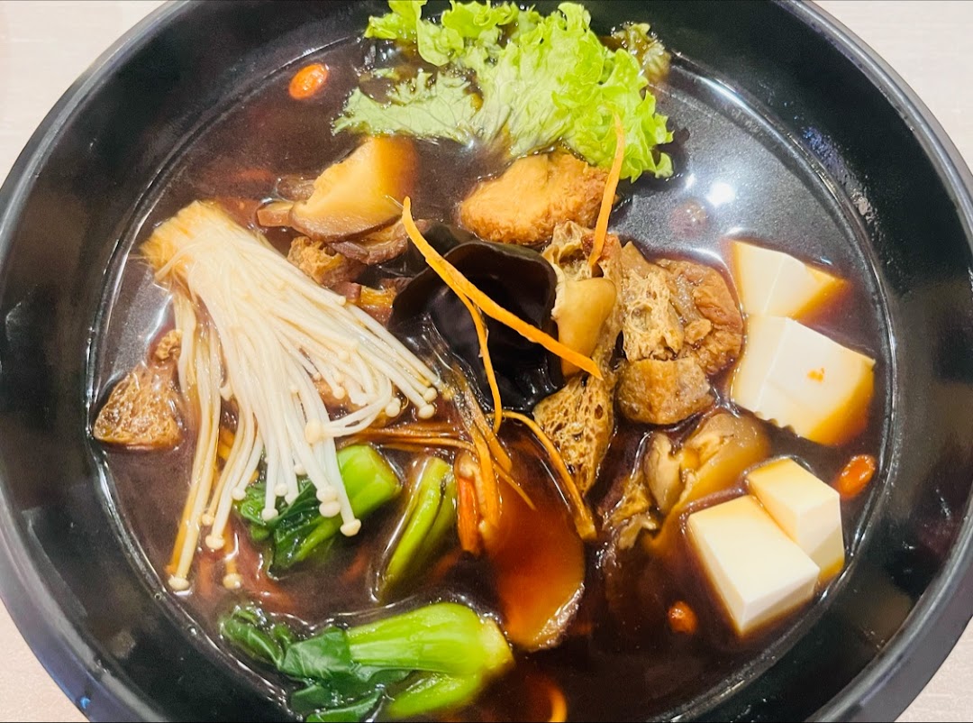 A close-up of a hearty, dark broth soup filled with mushrooms, tofu, and green vegetables in a black bowl.