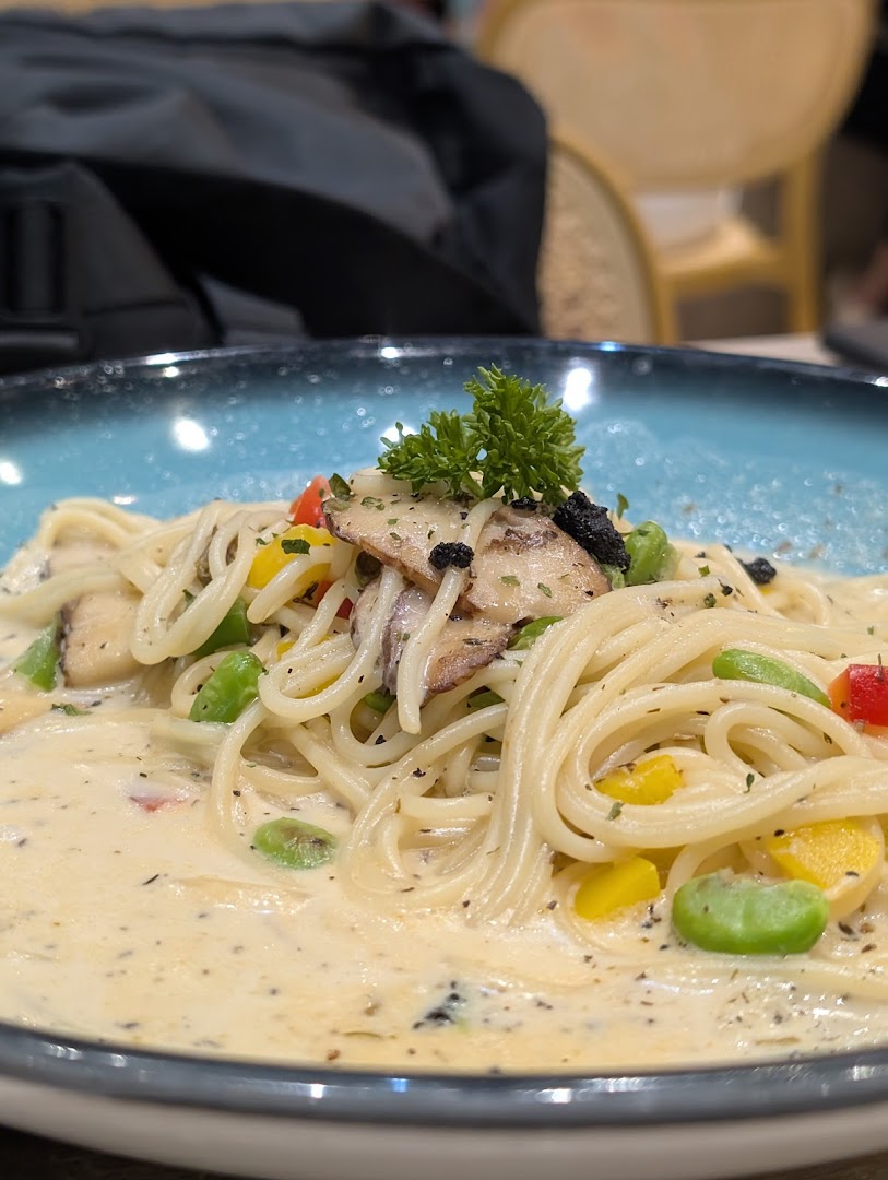 A close-up of creamy spaghetti pasta with mushrooms, bell peppers, and broad beans, garnished with parsley.