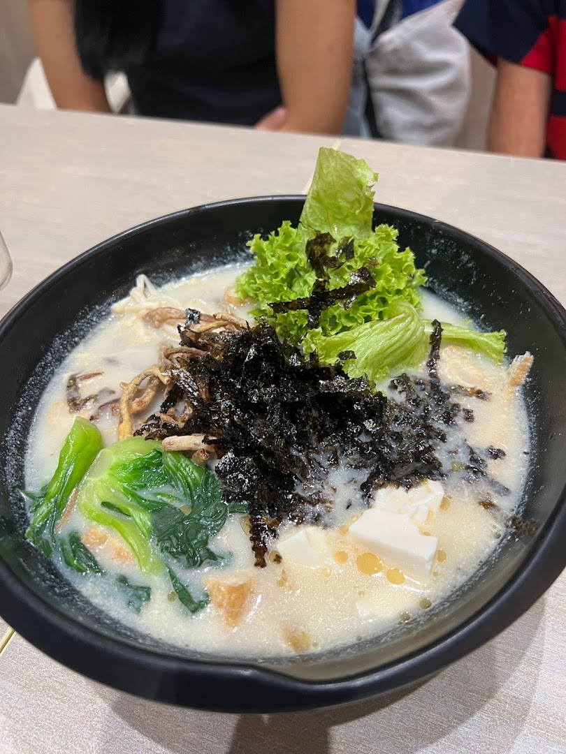 A close-up of a creamy soup dish topped with fresh lettuce, seaweed, tofu, and other ingredients.