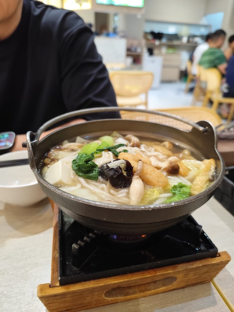 A steaming hotpot dish with vegetables, tofu, and noodles served on a table.