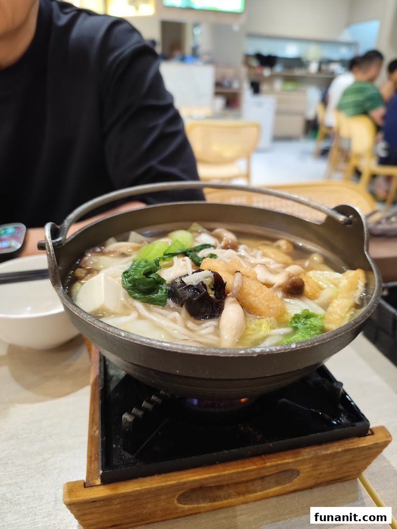 A steaming hotpot dish with vegetables, tofu, and noodles served on a table.