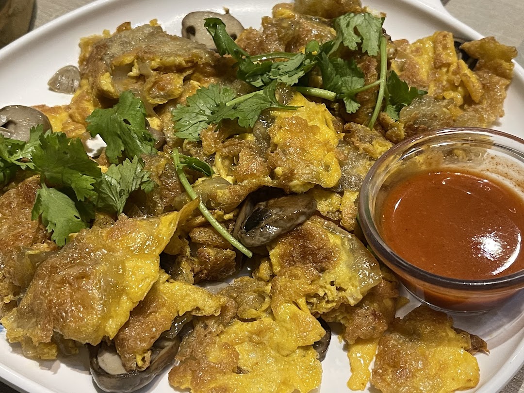A close-up of a golden-fried dish with mushrooms, garnished with fresh cilantro, served with a side of chili sauce.