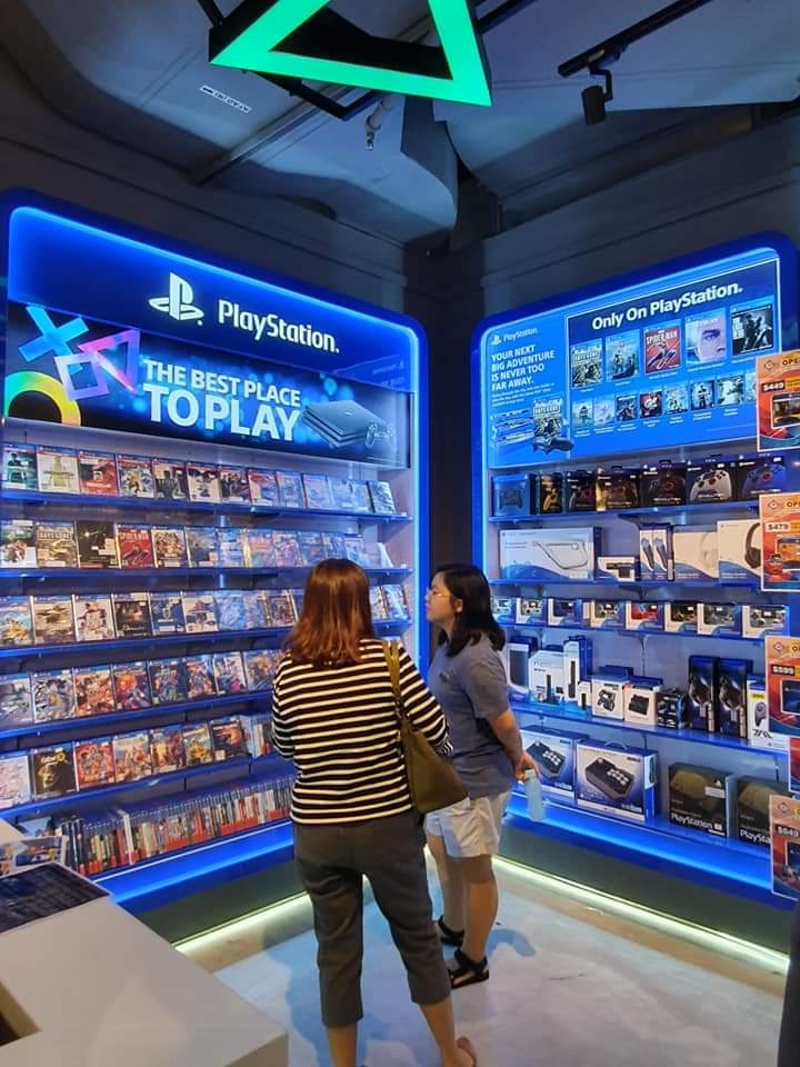 Two customers browse PlayStation games and accessories in a brightly lit display at GameMartz.