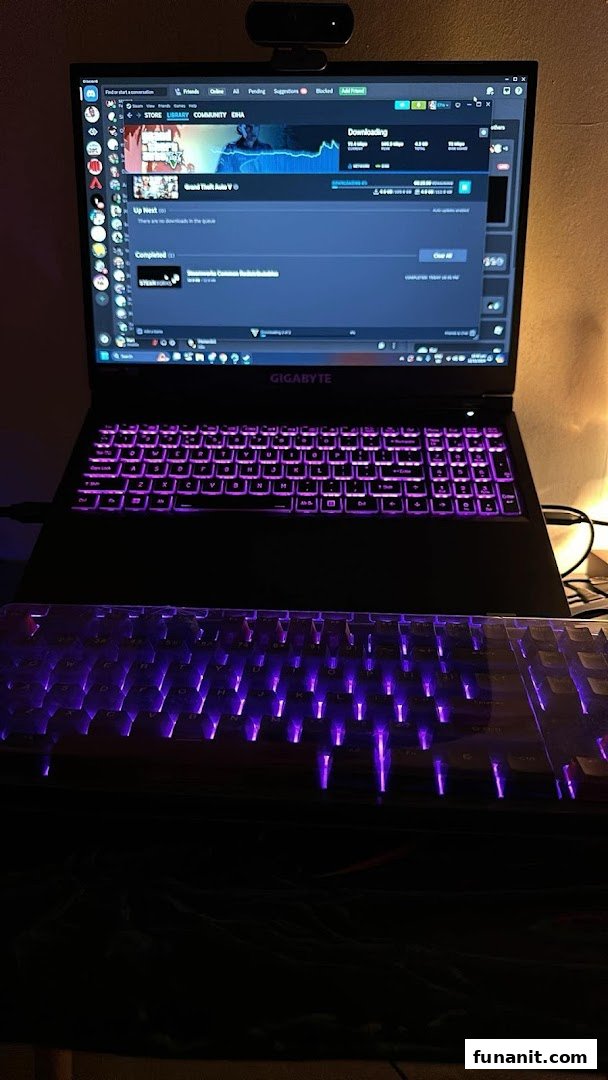 A gaming laptop and external keyboard with vibrant purple backlighting, displaying a game download on Steam.