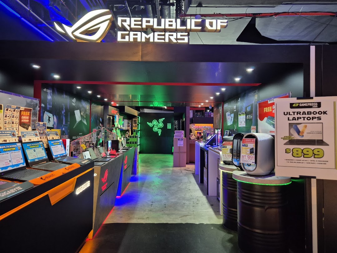 Illuminated entrance of GAMEPROSG, a gaming and laptop store, showcasing various tech displays.