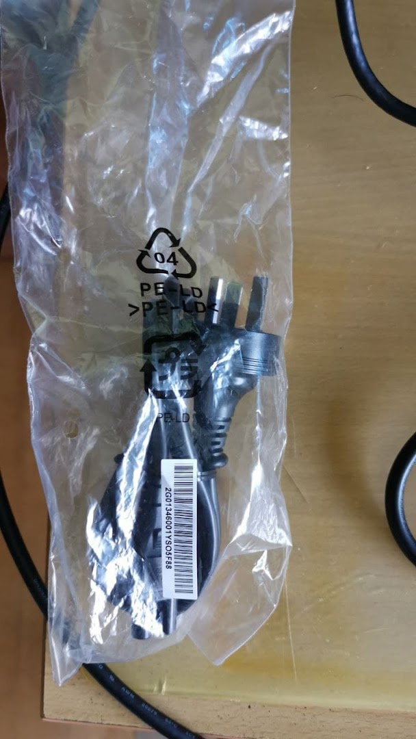 A black power cable with a UK plug, packaged in a clear plastic bag, likely an accessory.