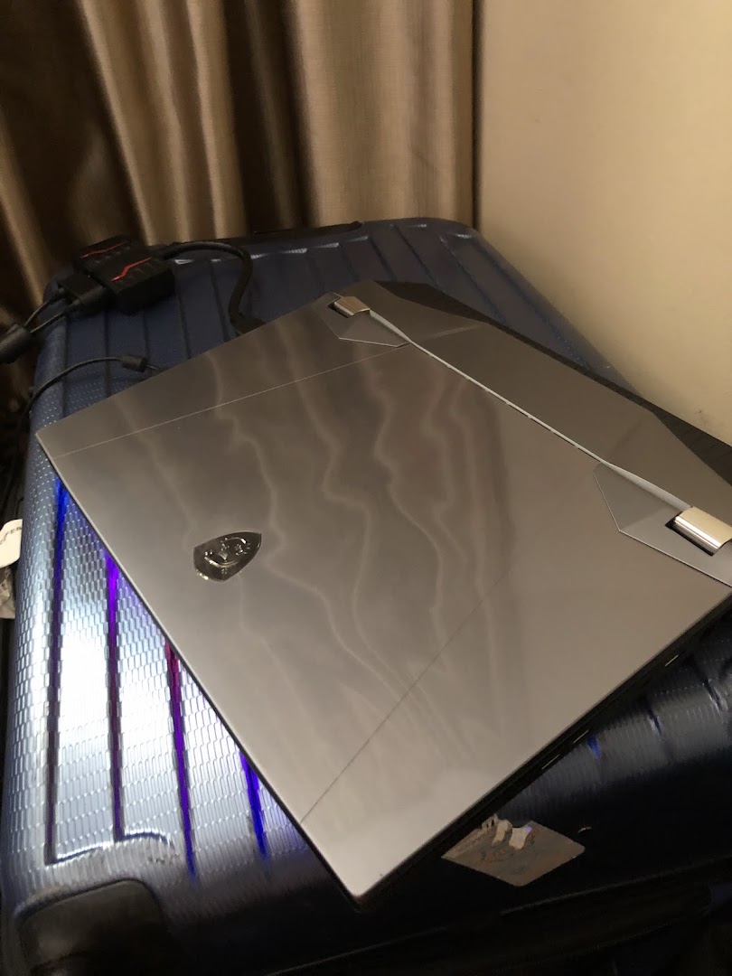 A sleek gaming laptop, possibly an MSI, rests on a suitcase with cables nearby.