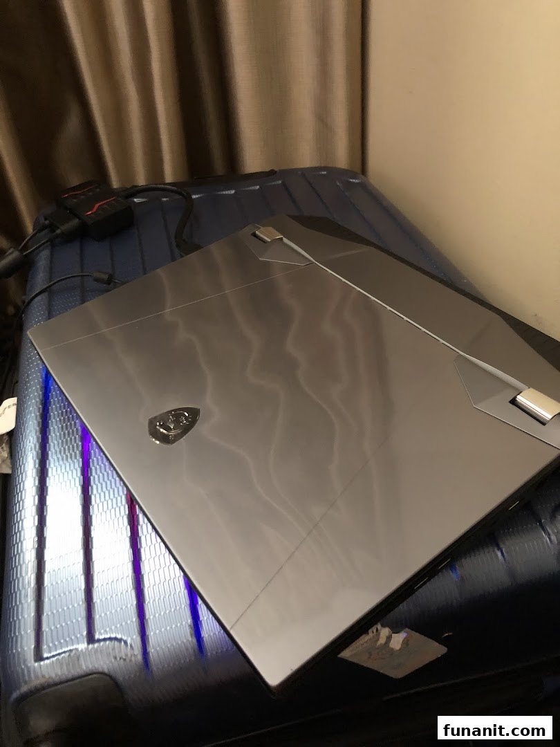A sleek gaming laptop, possibly an MSI, rests on a suitcase with cables nearby.
