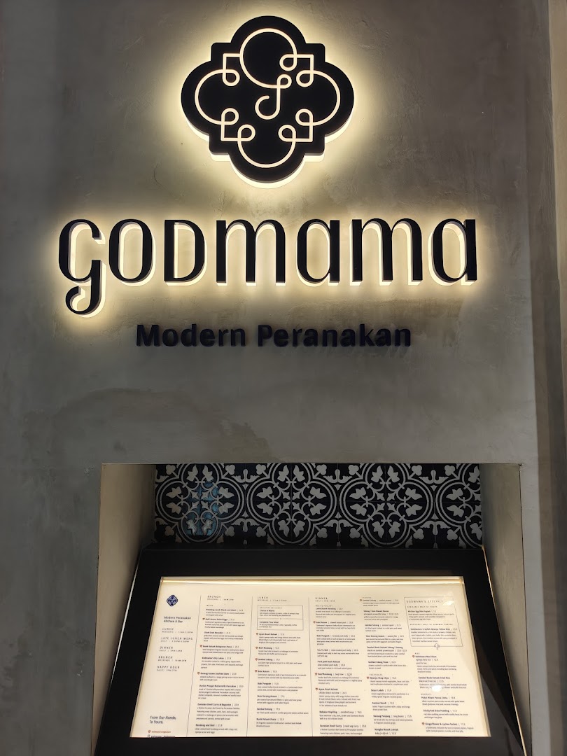 The illuminated Godmama restaurant sign and a display menu stand at its modern Peranakan entrance.