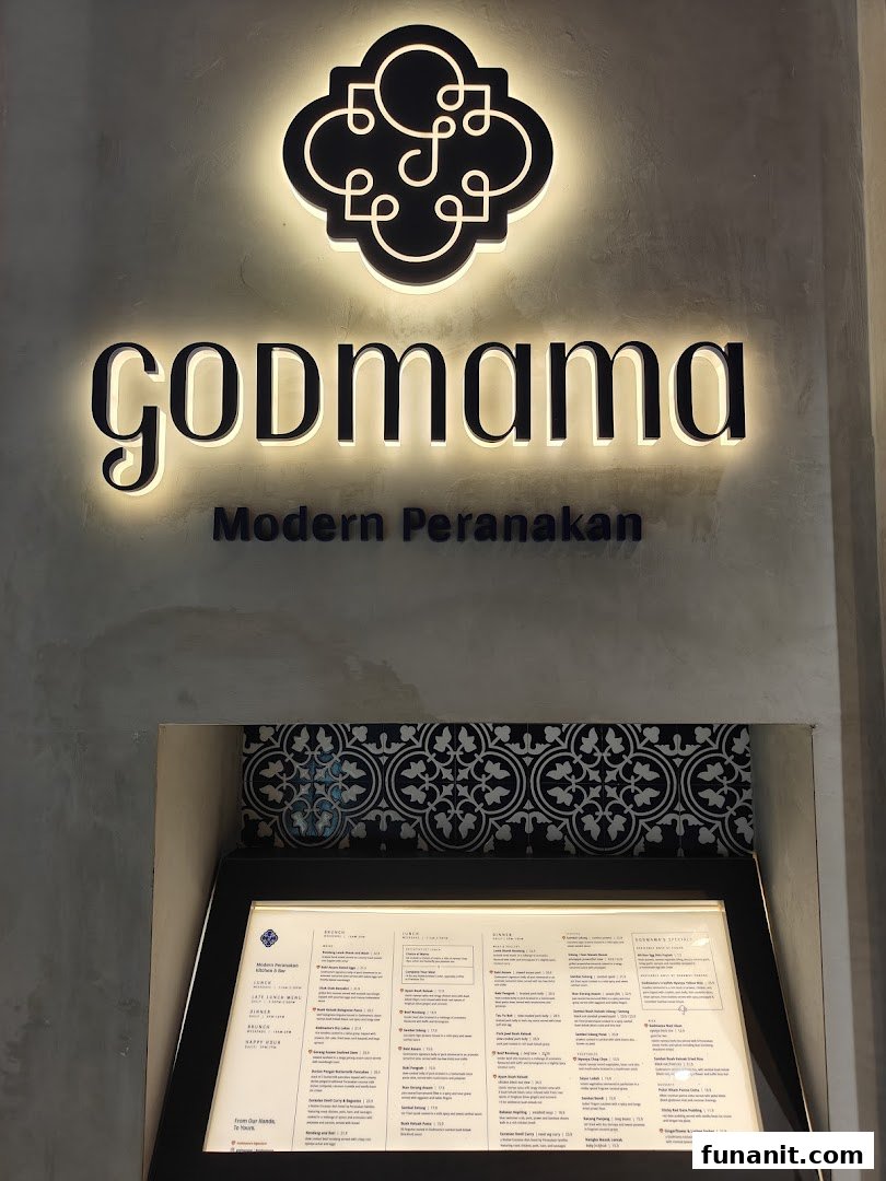 The illuminated Godmama restaurant sign and a display menu stand at its modern Peranakan entrance.