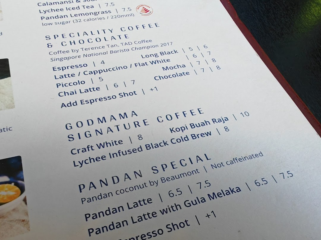 A close-up view of Godmama's beverage menu, featuring specialty coffees, signature drinks, and pandan specials.