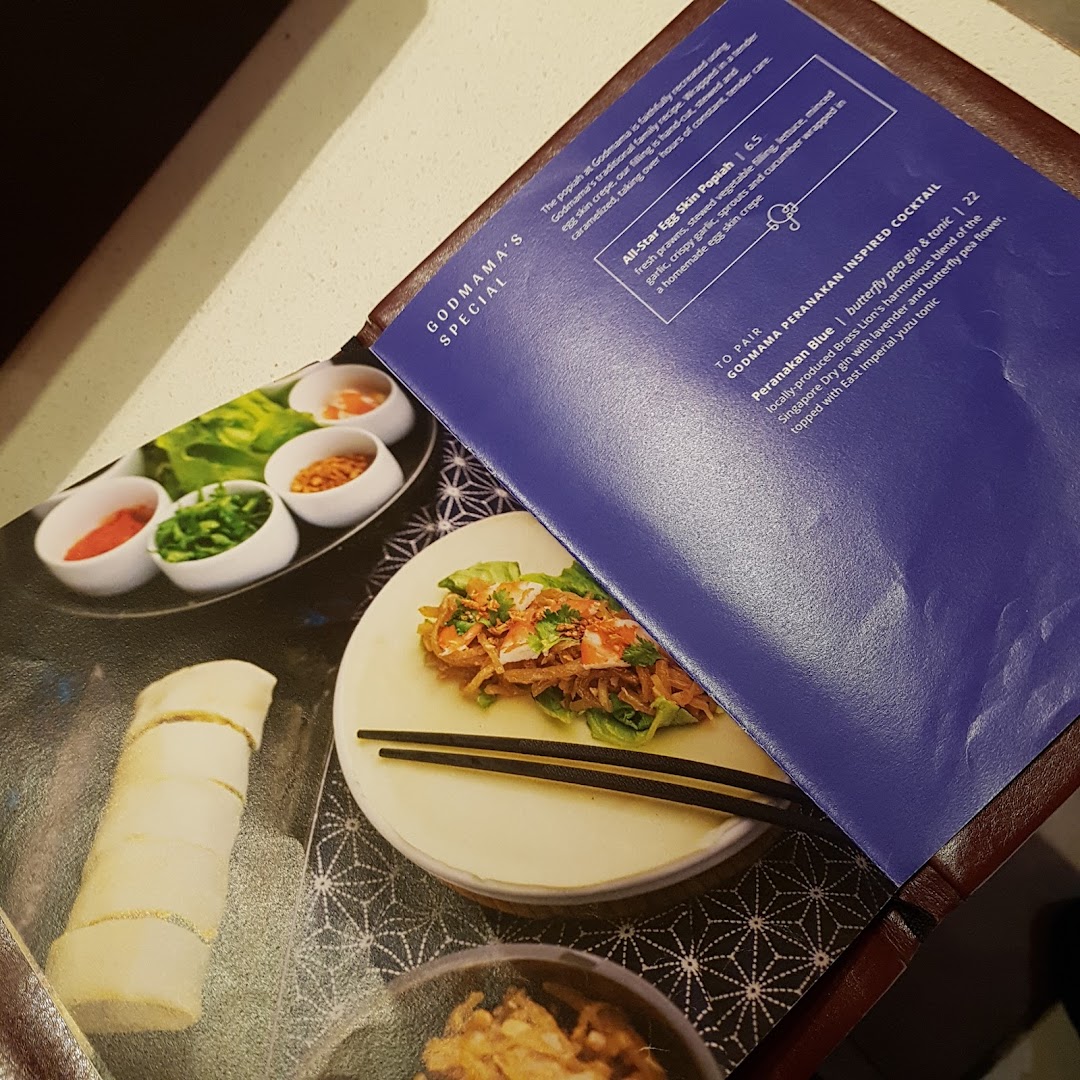 A close-up of Godmama's menu, showcasing a special popiah dish and a unique Peranakan-inspired cocktail.
