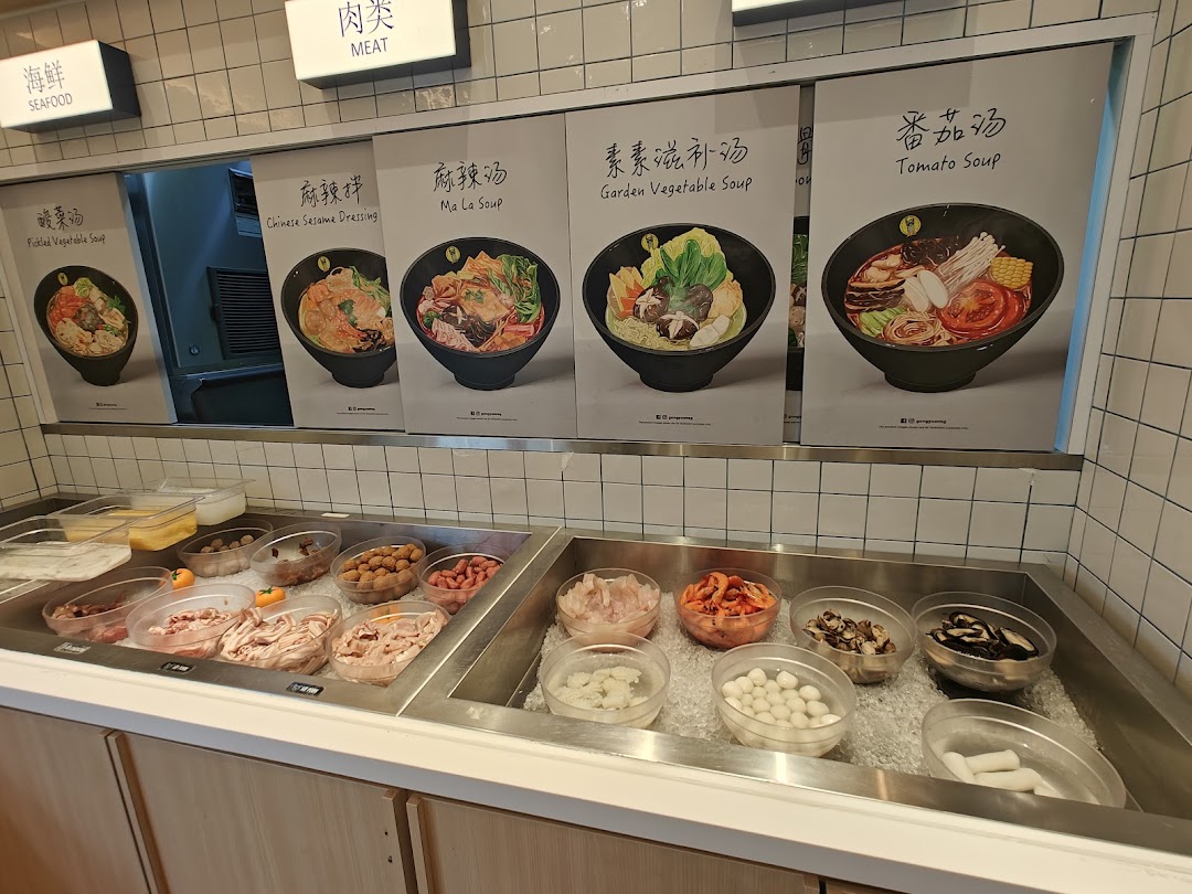 A self-service counter displaying fresh ingredients and posters of various customizable soup bases and a dry mix.