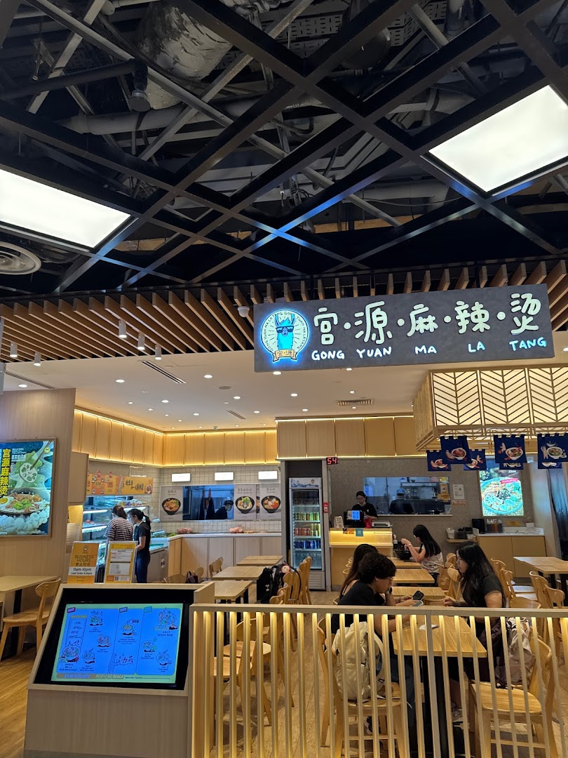 A bright and inviting interior view of Gong Yuan Ma La Tang, featuring wooden decor, seating, and a food preparation area.