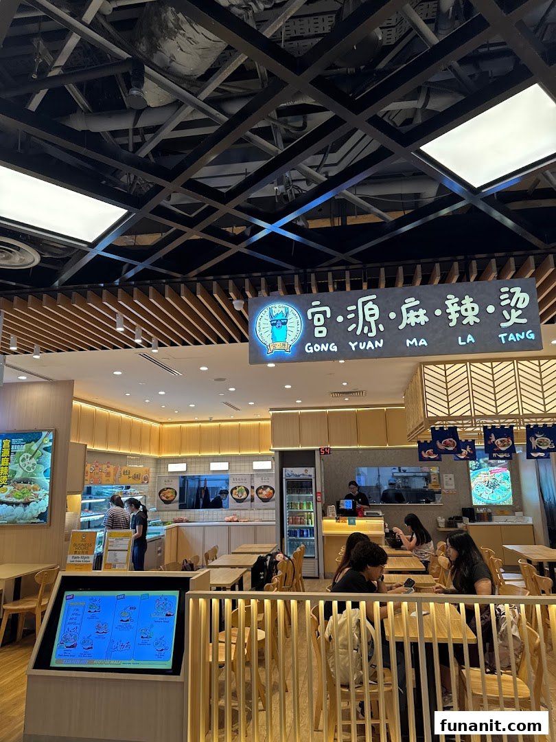 A bright and inviting interior view of Gong Yuan Ma La Tang, featuring wooden decor, seating, and a food preparation area.