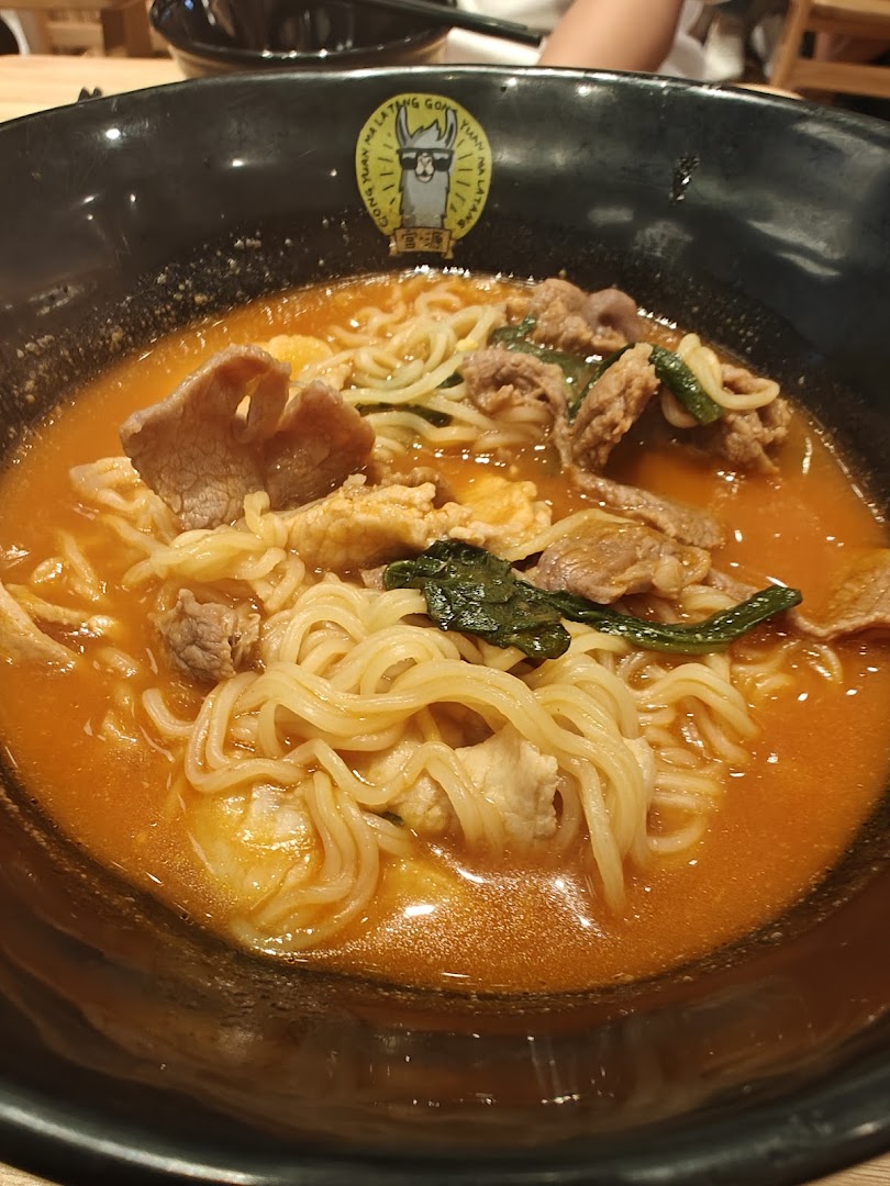 A close-up of a delicious bowl of Ma La Tang noodles with meat and vegetables in a rich broth.
